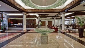 A spacious lobby with a central glass table, wooden columns, and a high ceiling with a green marble design. - Hotel Crocus (Zakopane)