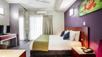 Habitación de hotel con cama, escritorio, silla, televisor, teléfono y un cuadro en la pared.