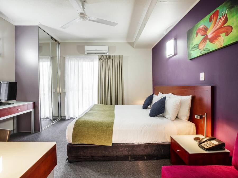 Habitación de hotel con cama, escritorio, silla, televisor, teléfono y un cuadro en la pared.