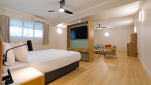 A modern hotel room with a bed, desk, chair, TV, ceiling fan, and wooden flooring. - Novotel Darwin Airport (Eaton)