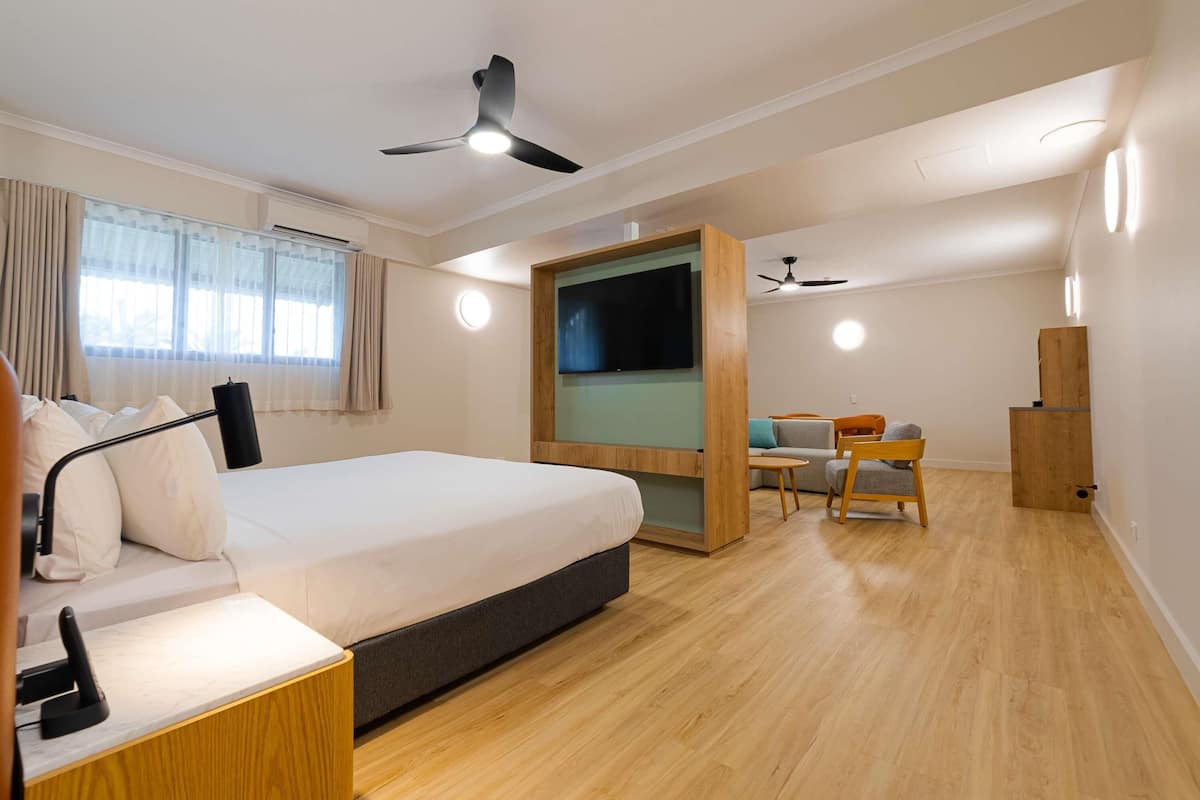 Una habitación de hotel moderna con cama, escritorio, silla, televisor, ventilador de techo y suelo de madera.