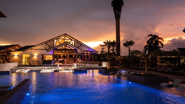 A swimming pool with a modern building and a tall tower in the background. - Novotel Darwin Airport (Eaton)