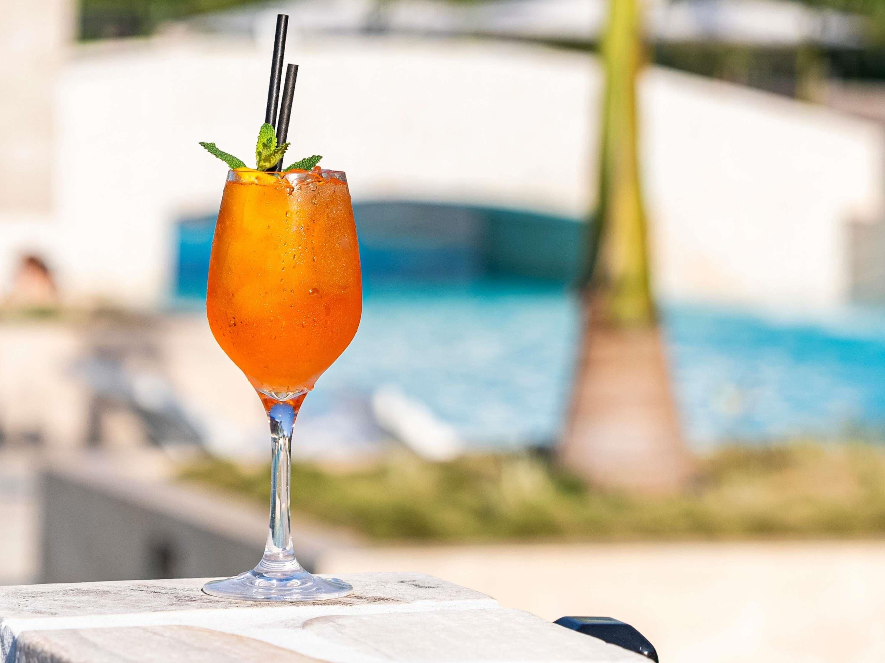 A cocktail glass with a straw and mint garnish on a table by a poolside.