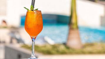 A cocktail glass with a straw and mint garnish on a table by a poolside.
