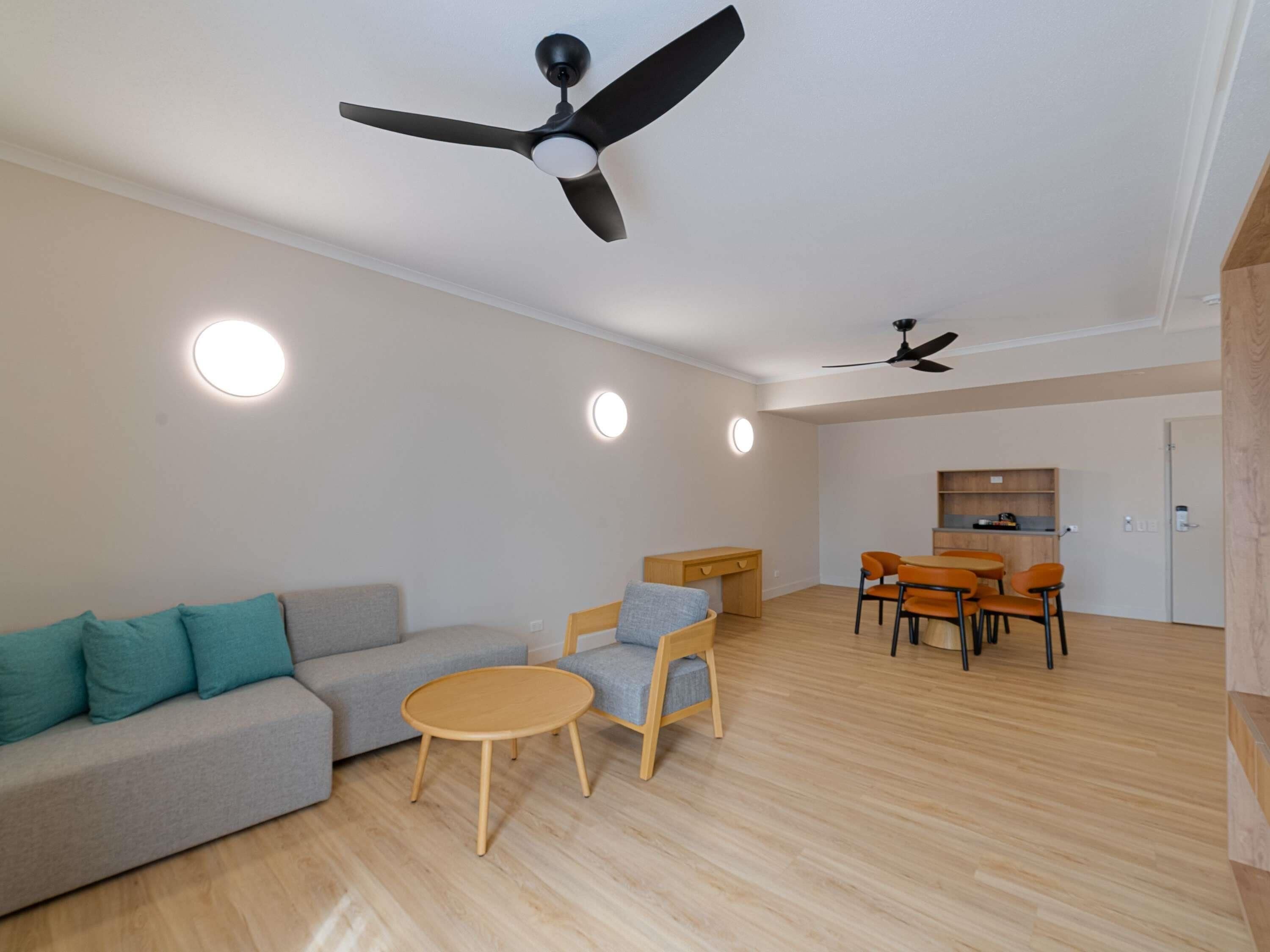 Una sala de estar moderna con un sofá, una mesa redonda de madera, un comedor con sillas y dos ventiladores de techo.
