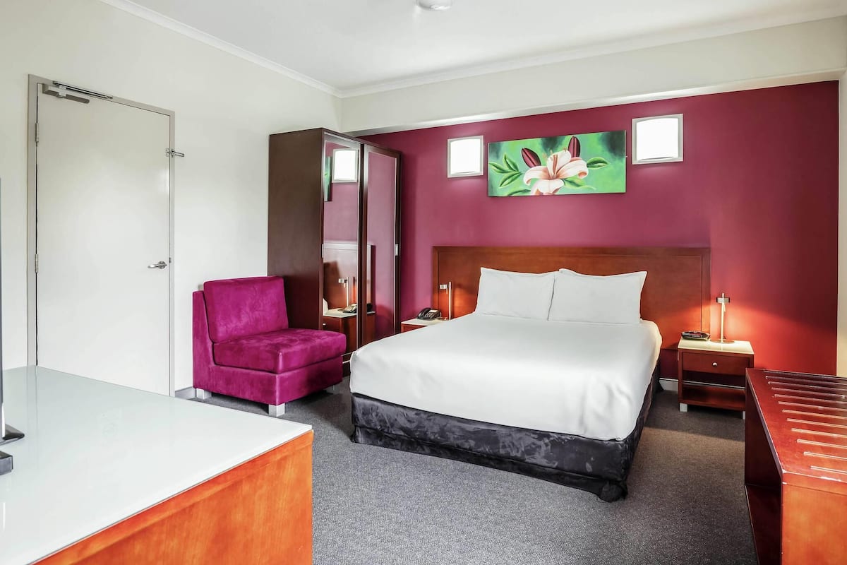 Una habitación de hotel con cama, escritorio, silla, armario y mesita de noche.