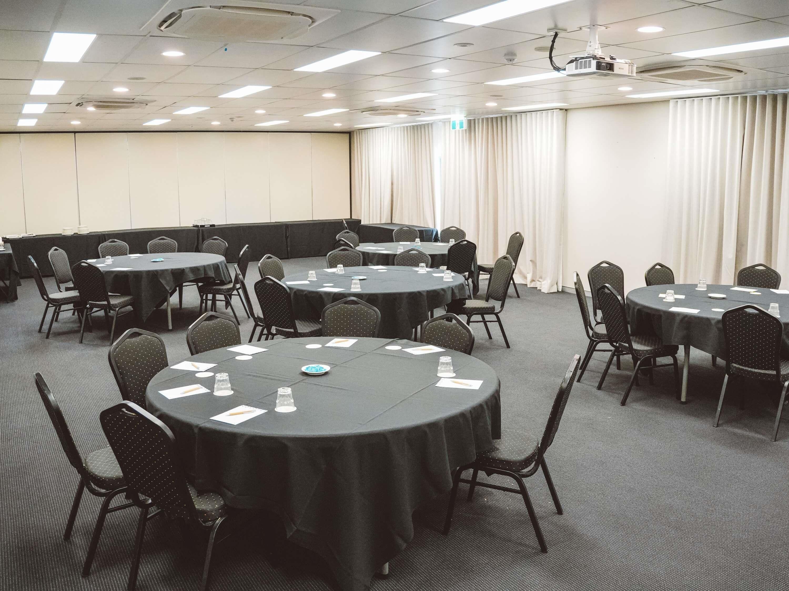 A conference room with multiple round tables, chairs, and a projector.