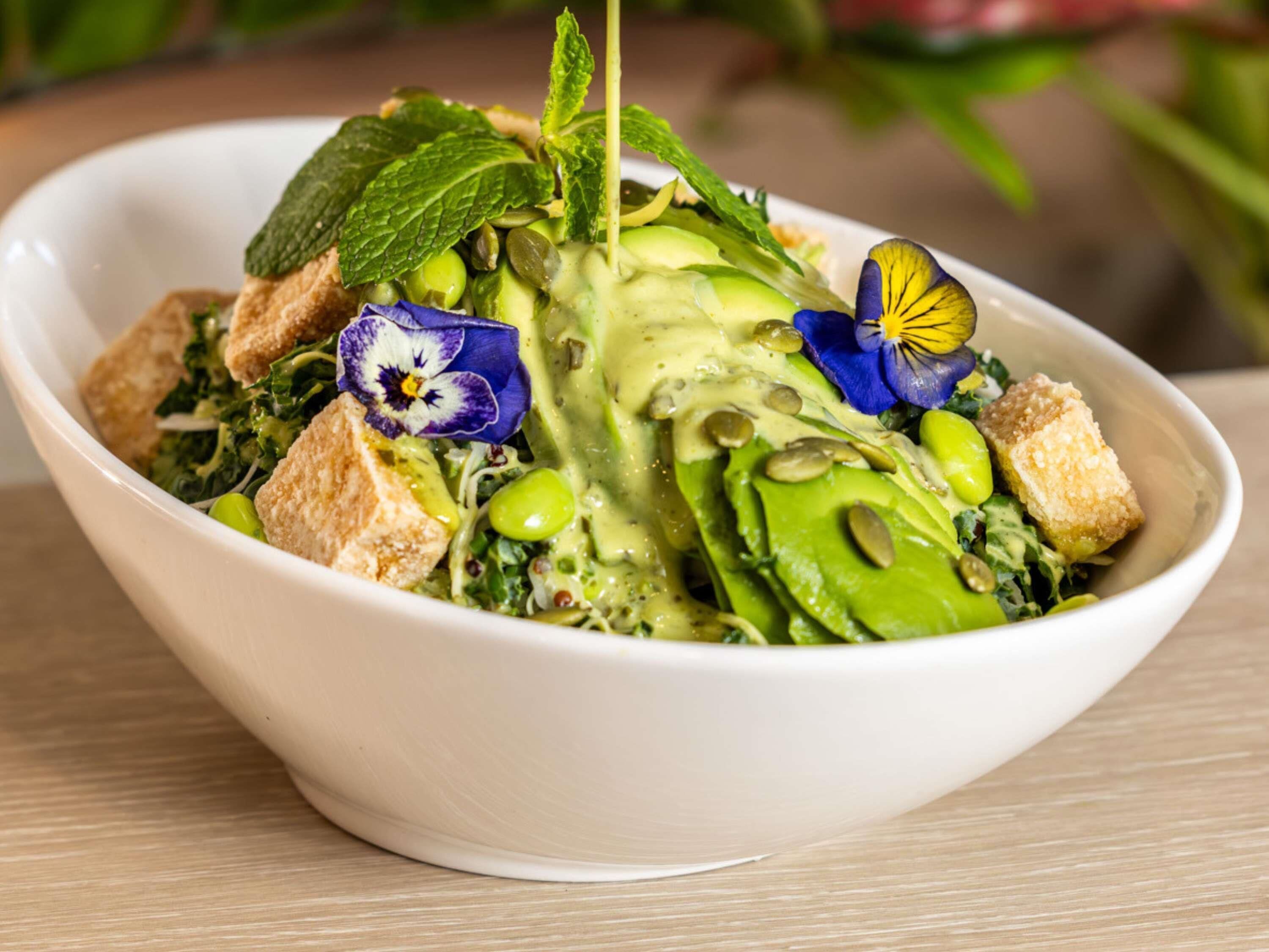 Ensalada en un bol con diversas verduras, crutones y un chorrito de aderezo.