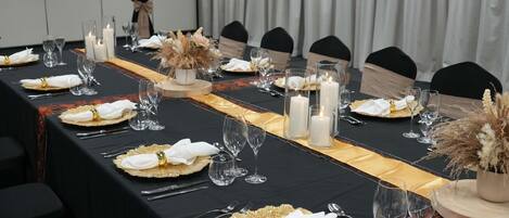 Una larga mesa de comedor dispuesta con servilletas blancas, detalles dorados y velas.