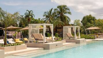 A poolside area with lounge chairs and umbrellas, surrounded by palm trees and a clear sky.