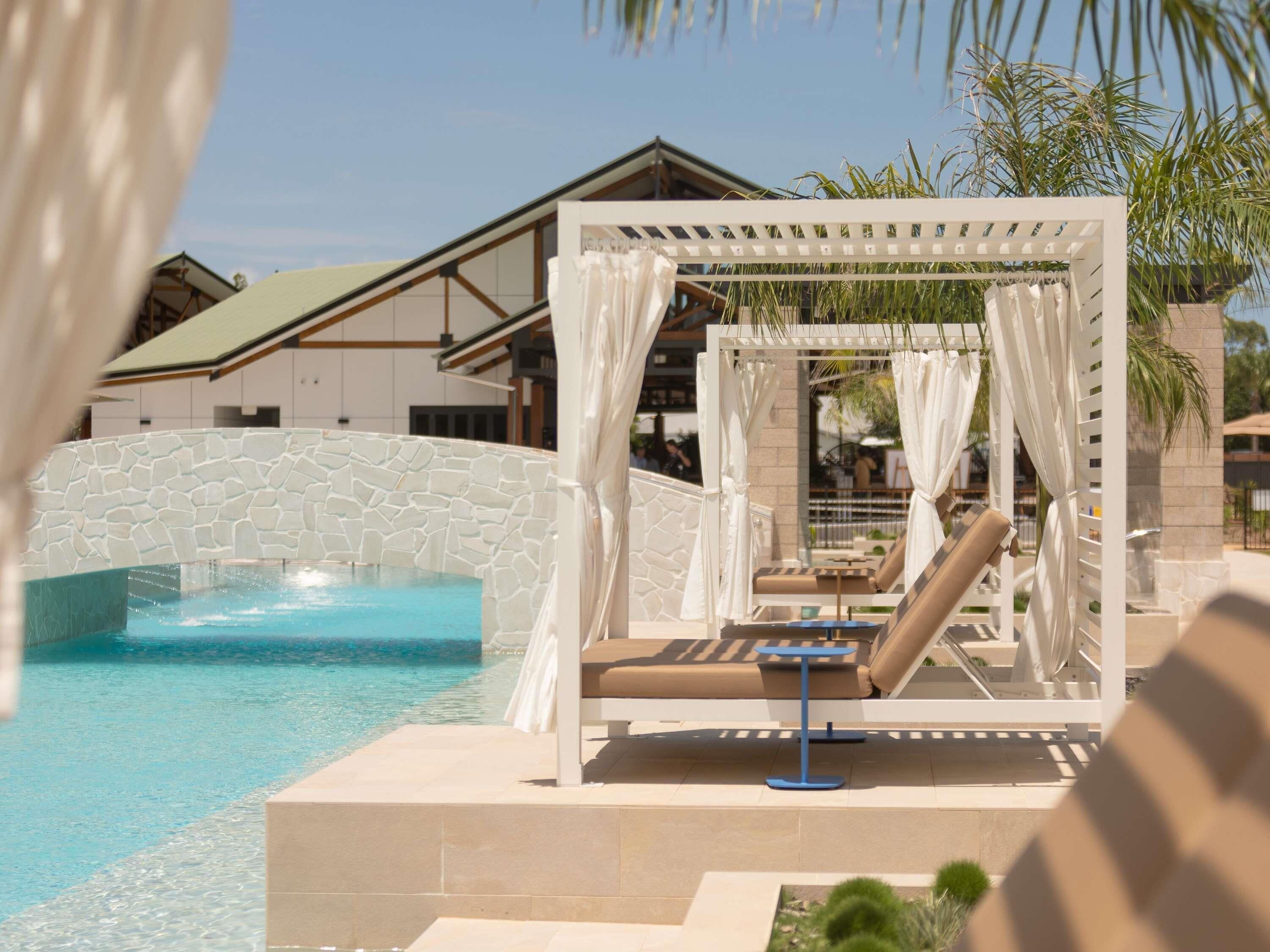 A pool area with a stone wall, a water feature, and a covered seating area with a table.