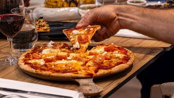 En pizza på en träbricka, och en hand som plockar upp en bit.