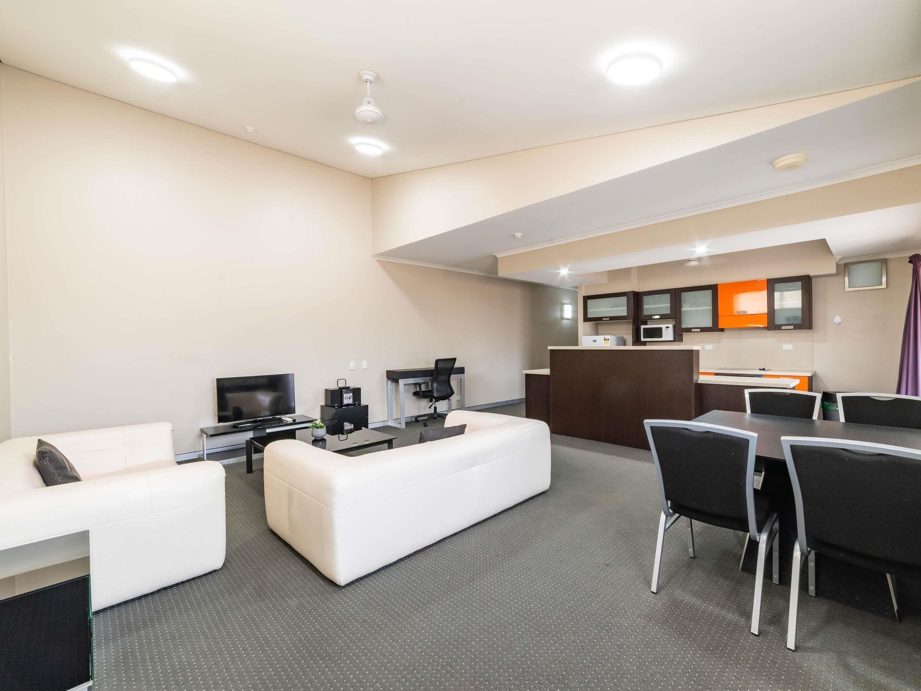 A modern hotel room with a living area, a dining table, and a kitchenette.