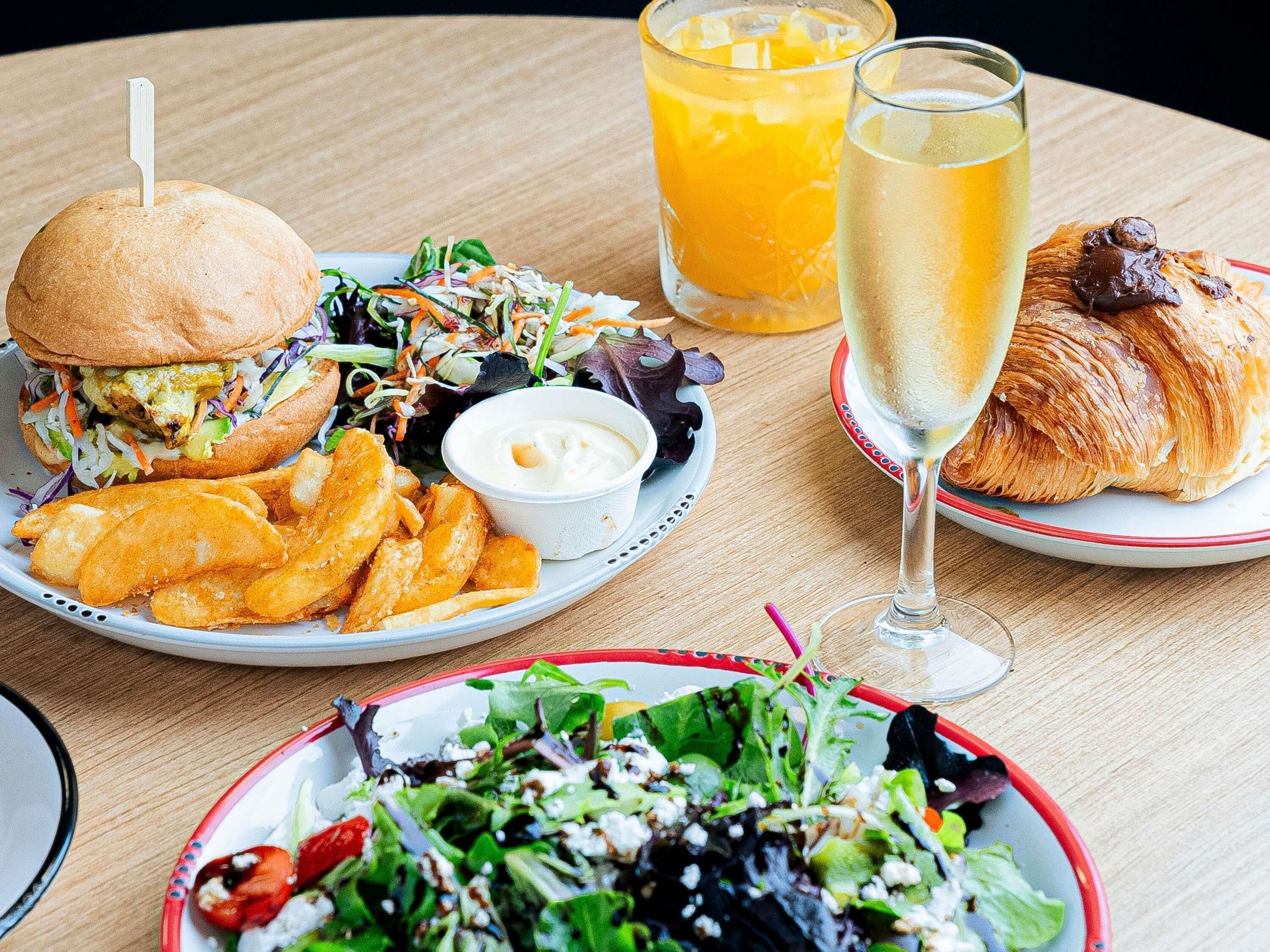 A table with a burger, salad, fries, a croissant, and two glasses of orange juice.