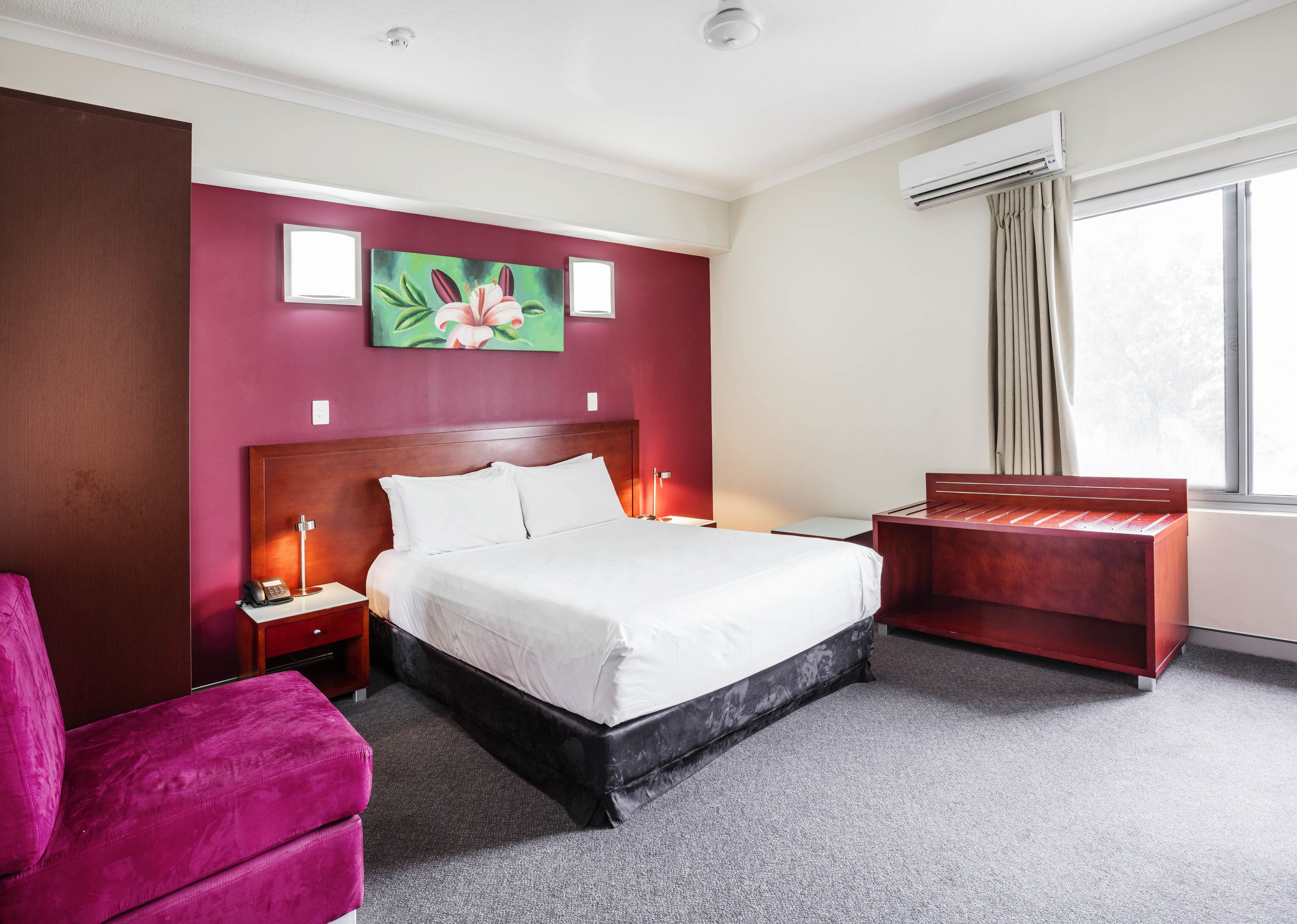 A hotel room with a large bed, a desk, a chair, and a window with curtains.