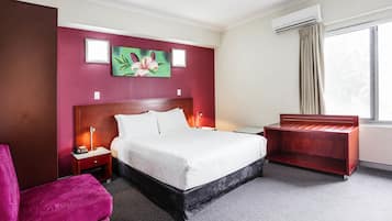 A hotel room with a large bed, a desk, a chair, and a window with curtains.