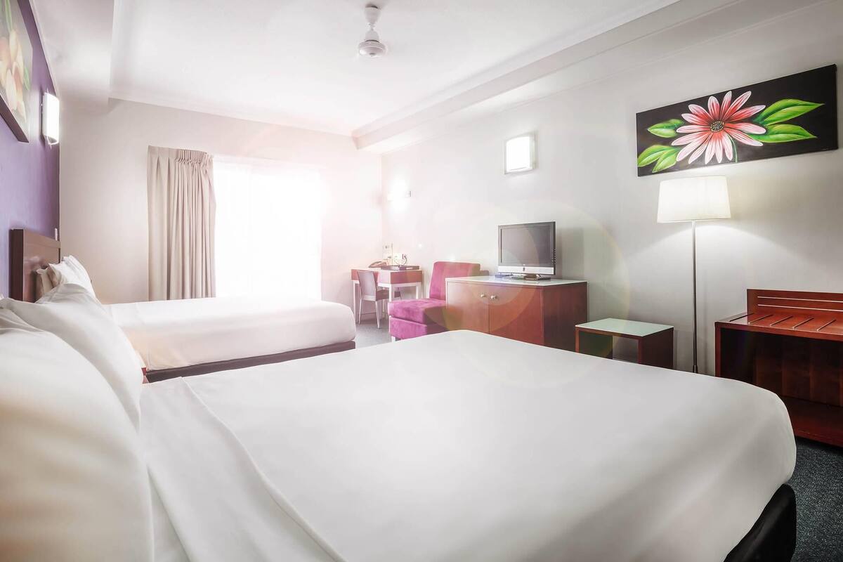 Una habitación de hotel con dos camas, un escritorio, una silla, un televisor y un cuadro en la pared.
