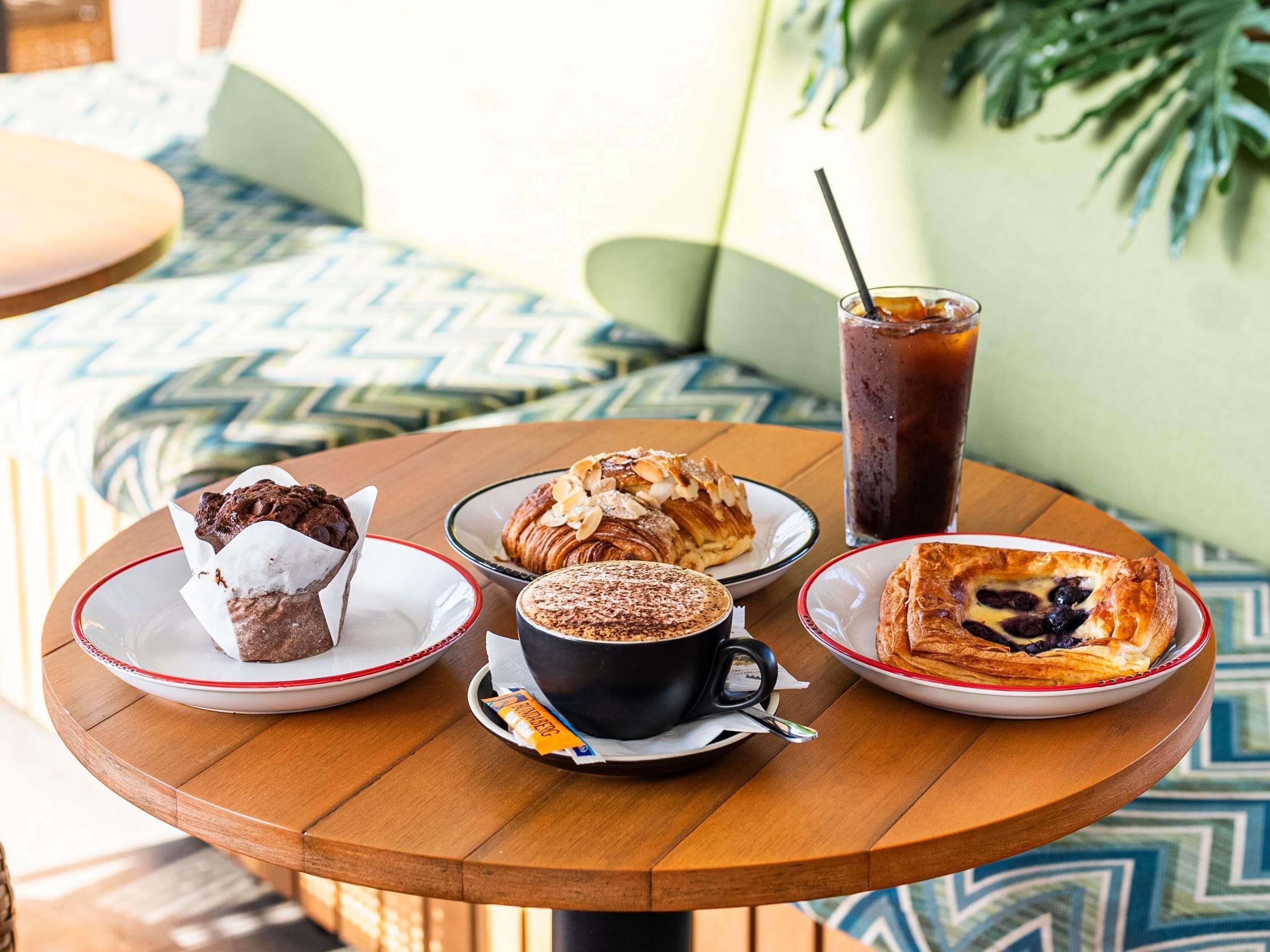 Una mesa de madera redonda con cuatro platos de comida, una taza de café y un vaso alto de té helado.