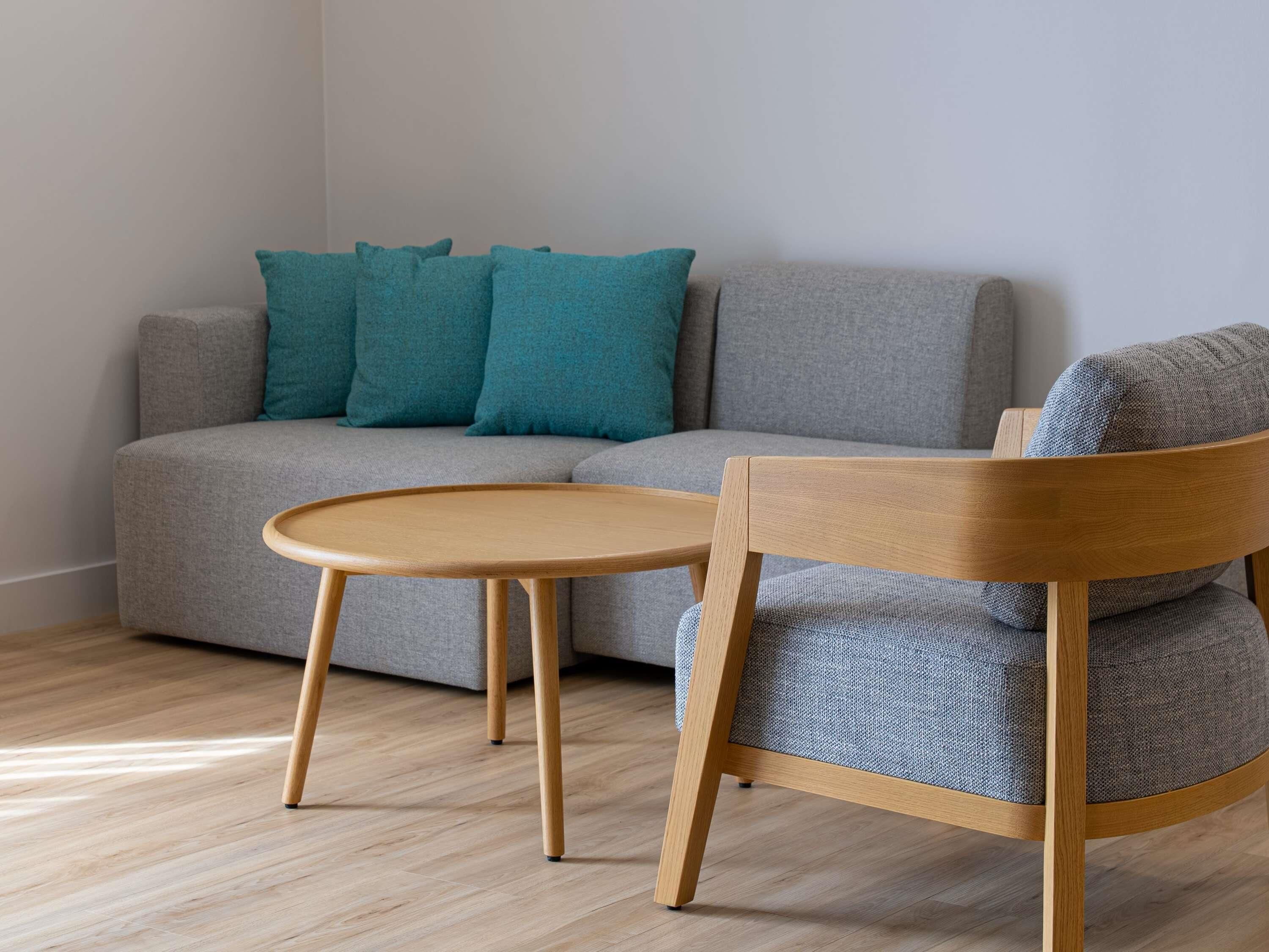 Una sala de estar moderna con un sofá gris, cojines azul verdosos, una silla de madera y una pequeña mesa de madera.