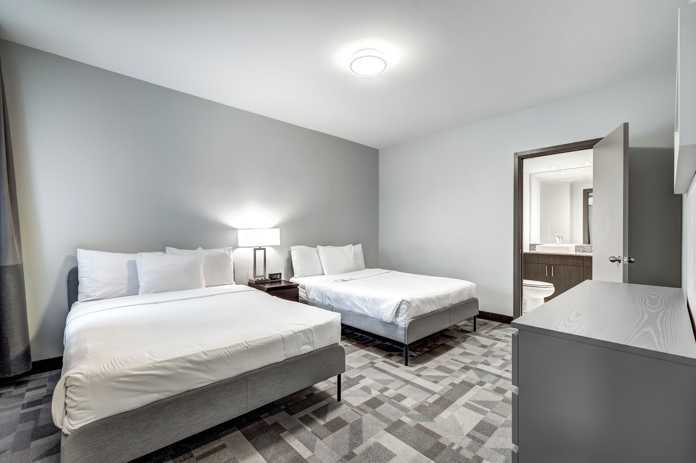 A hotel room with two beds, a nightstand, a mirror, and a bathroom visible through an open door.