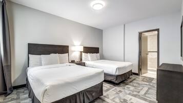 Habitación de hotel con dos camas, una mesita de noche, una lámpara, un aparador y la puerta del baño.