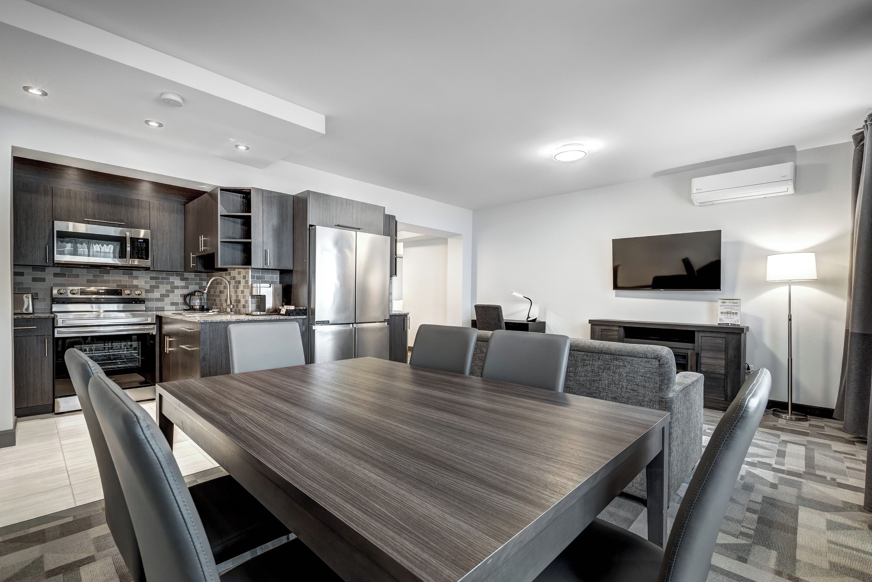 A modern kitchen with built-in appliances, a dining area with a large table and chairs, and a flat-screen TV mounted on the wall.