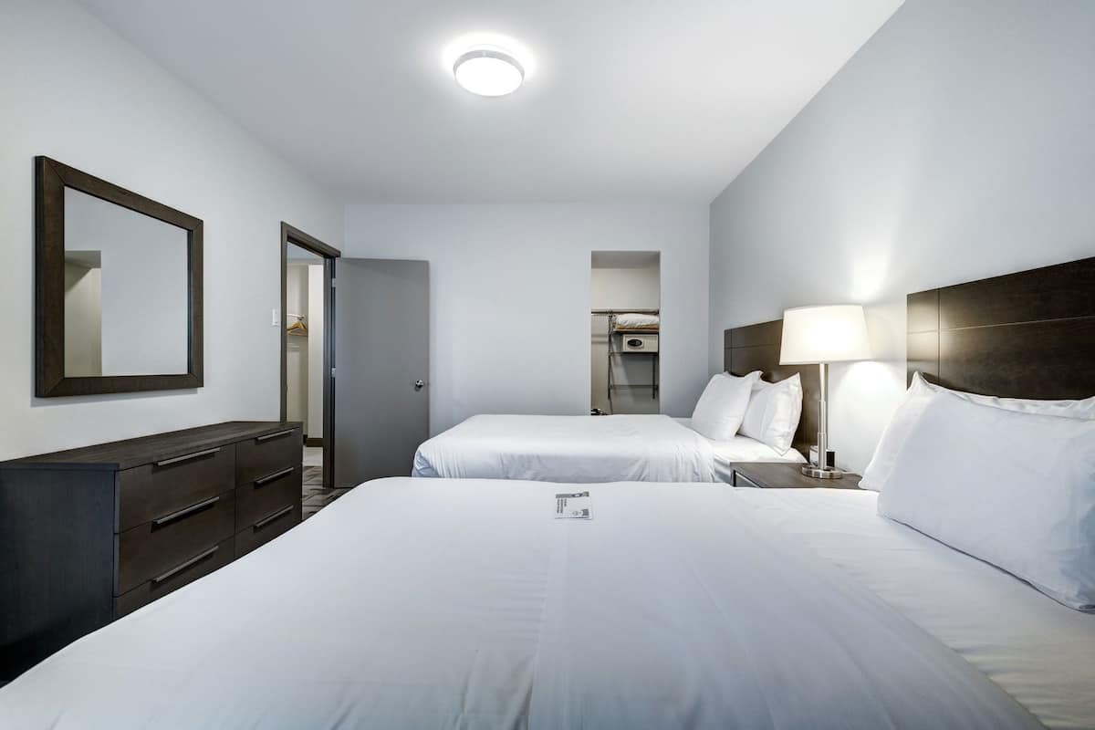 A hotel room with two beds, a dresser, a mirror, and a lamp.