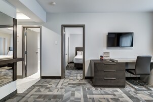 Une chambre d’hôtel comprenant un lit, un bureau avec des tiroirs, une chaise, un téléviseur à écran plat fixé au mur et une moquette à motifs.