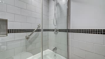 Un baño moderno con azulejos blancos, ducha con cerramiento de vidrio y una franja decorativa de azulejos en blanco y negro.