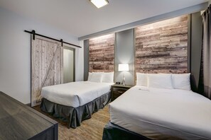 Habitación de hotel con dos camas, un panel decorativo de madera, una puerta corredera y una mesita de noche con lámpara.
