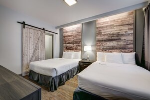 Une chambre d’hôtel avec deux lits, un mur décoratif en bois, une porte coulissante et une table de chevet avec une lampe.