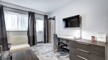 A hotel room with a sofa, a desk with drawers, a flat-screen TV, and a window with curtains.