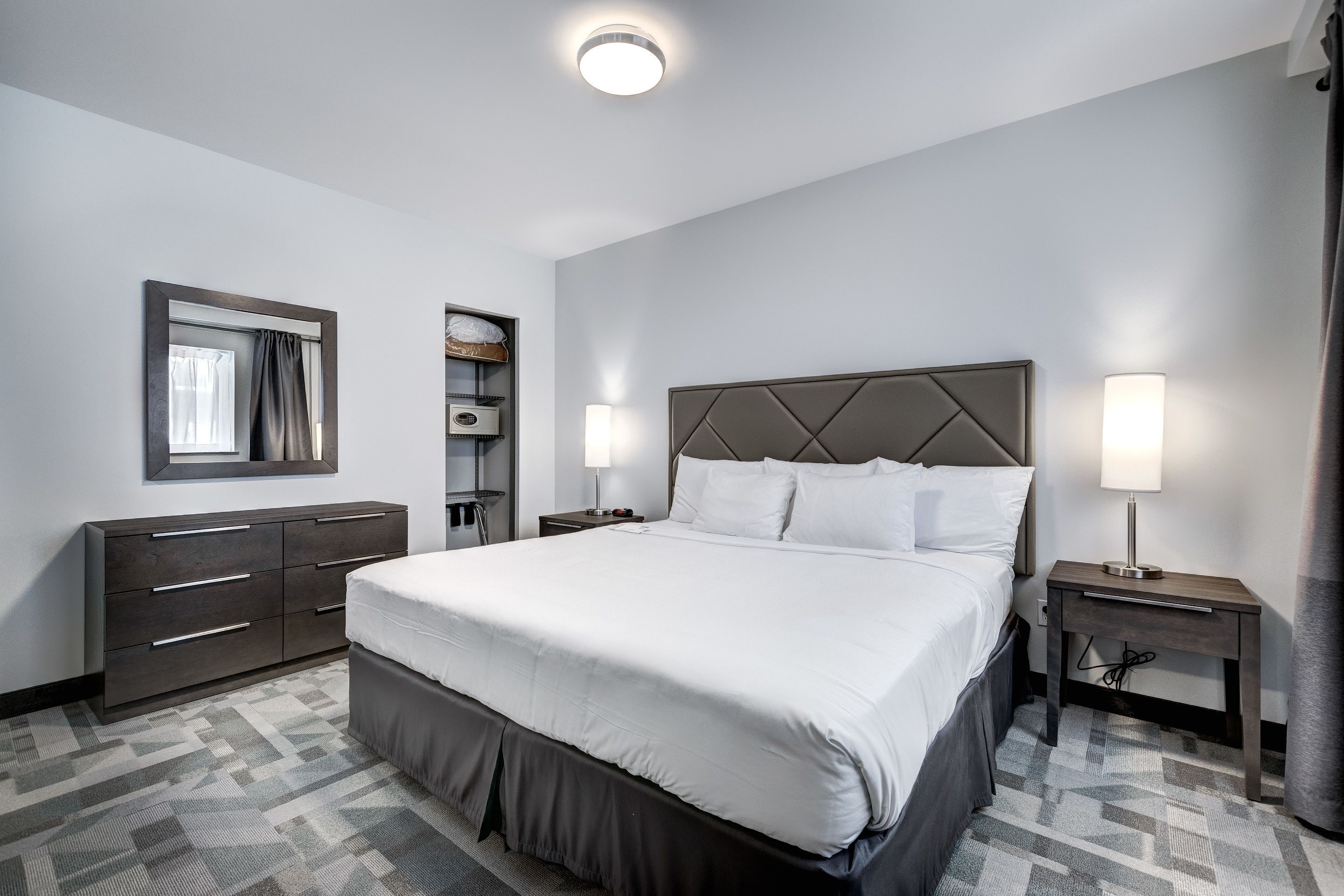 Una habitación de hotel con una cama grande, un tocador, un espejo y una mesita de noche con una lámpara.