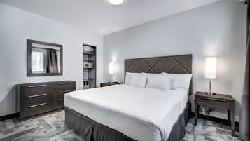 Una habitación de hotel con una cama grande, un tocador, un espejo y una mesita de noche con una lámpara.