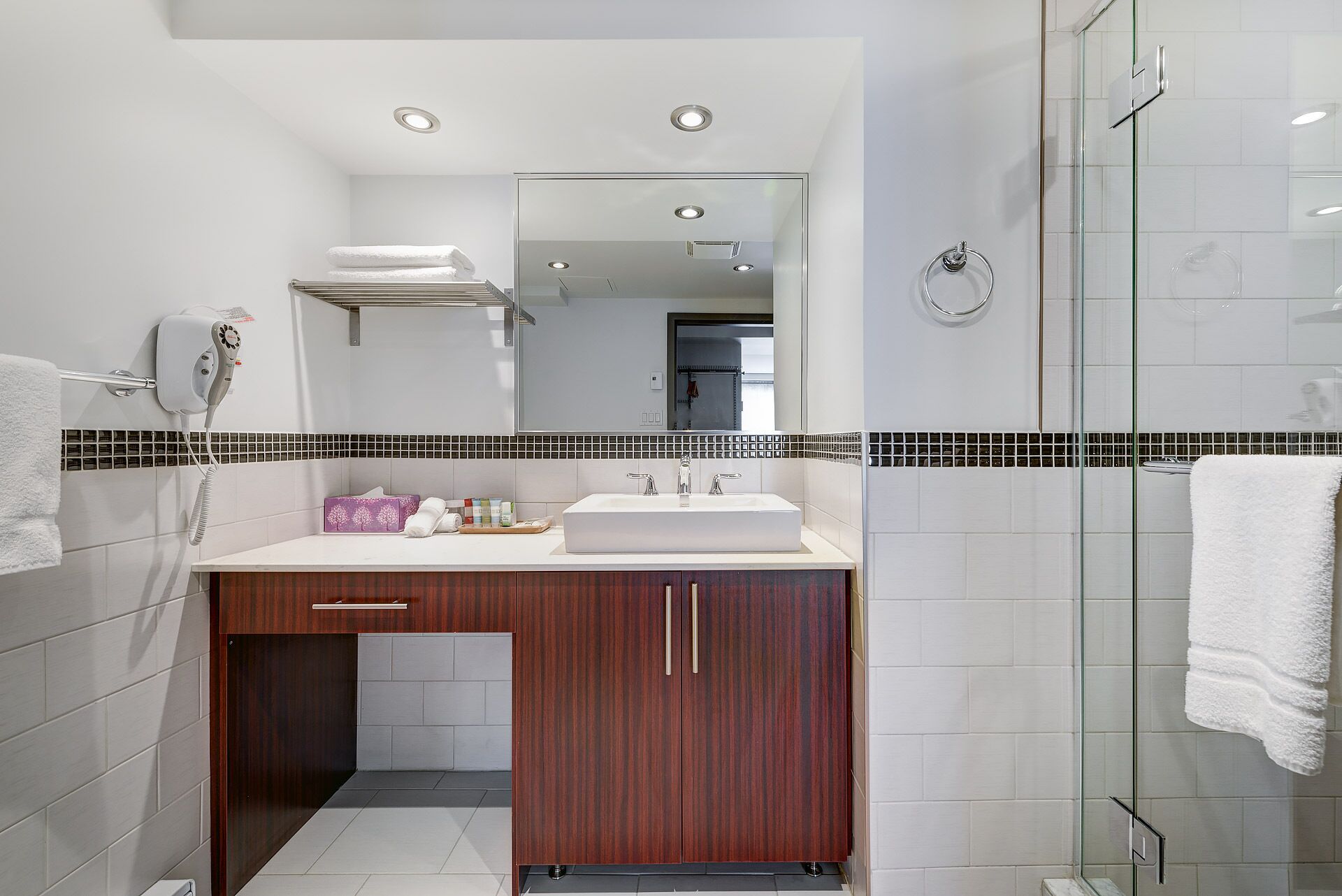 A modern bathroom with a white sink, wooden vanity, and a glass shower enclosure.