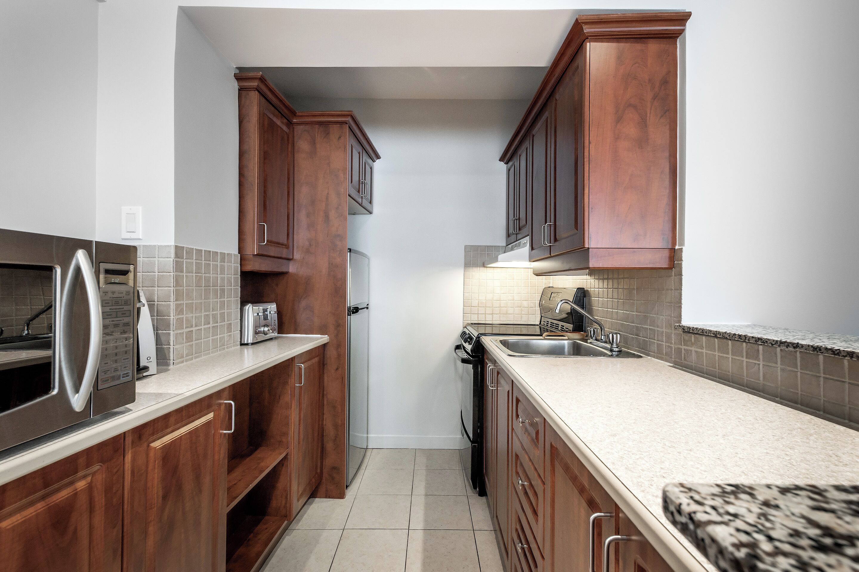 Una cocina con armarios de madera, un refrigerador de acero inoxidable, un microondas, un tostador y un lavavajillas.
