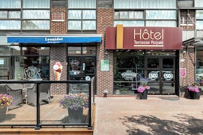 Entrada de un hotel con un cartel que dice "Hôtel Terrasse Royale" y un toldo azul sobre un restaurante llamado "Leonidas".