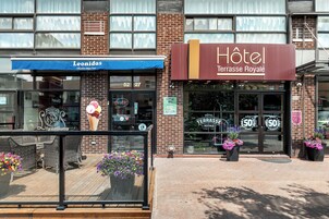L’entrée d’un hôtel, avec une enseigne indiquant « Hôtel Terrasse Royale » et un auvent bleu au-dessus d’un restaurant appelé « Leonidas ».