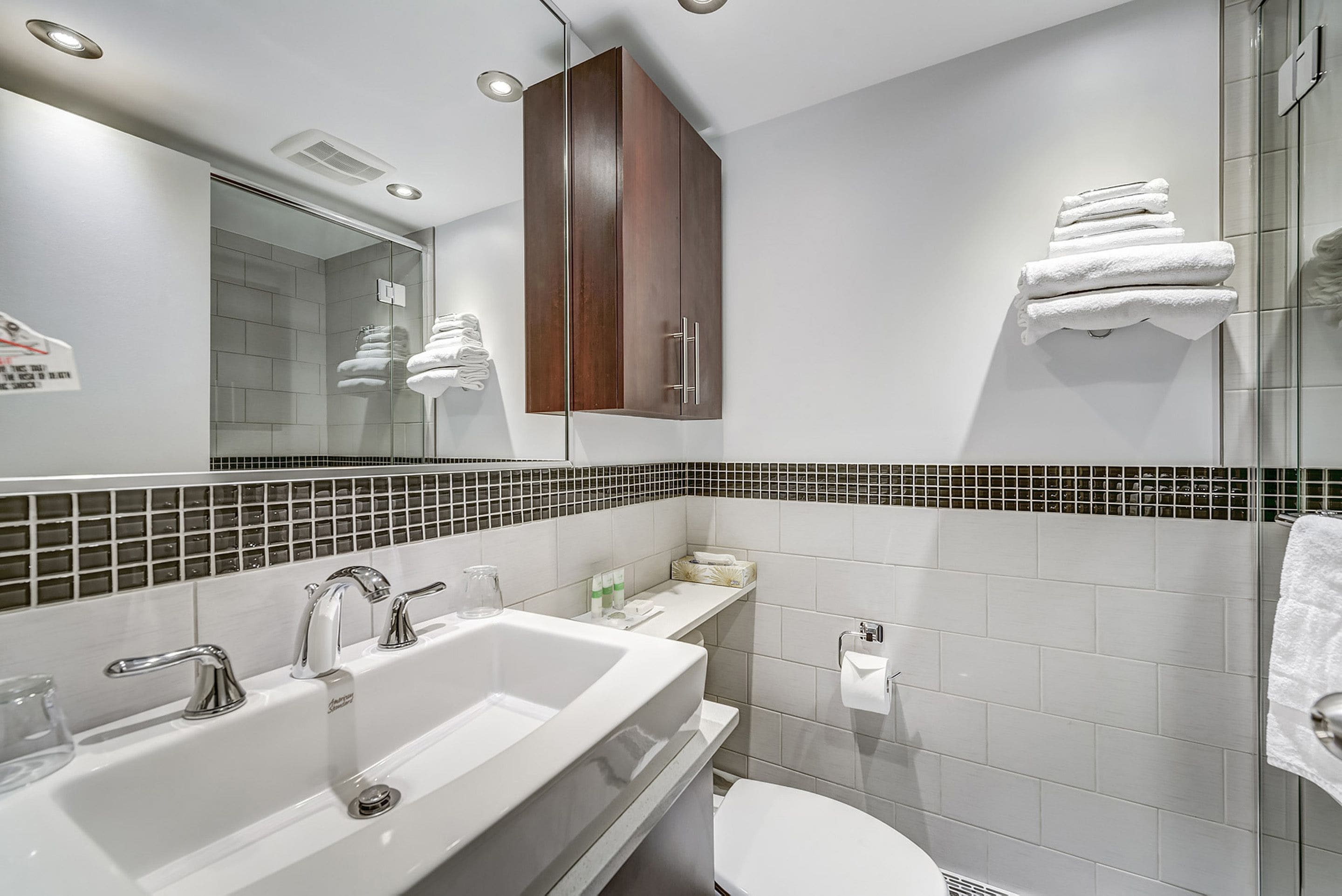 Un baño moderno con un espejo grande, un lavabo blanco y una cabina de ducha de vidrio.
