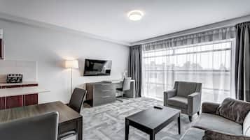 A modern hotel room with a dining area, a sofa, a TV, and a large window with curtains.