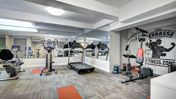 A modern hotel fitness center with cardio machines, weightlifting equipment, and a mirrored wall.