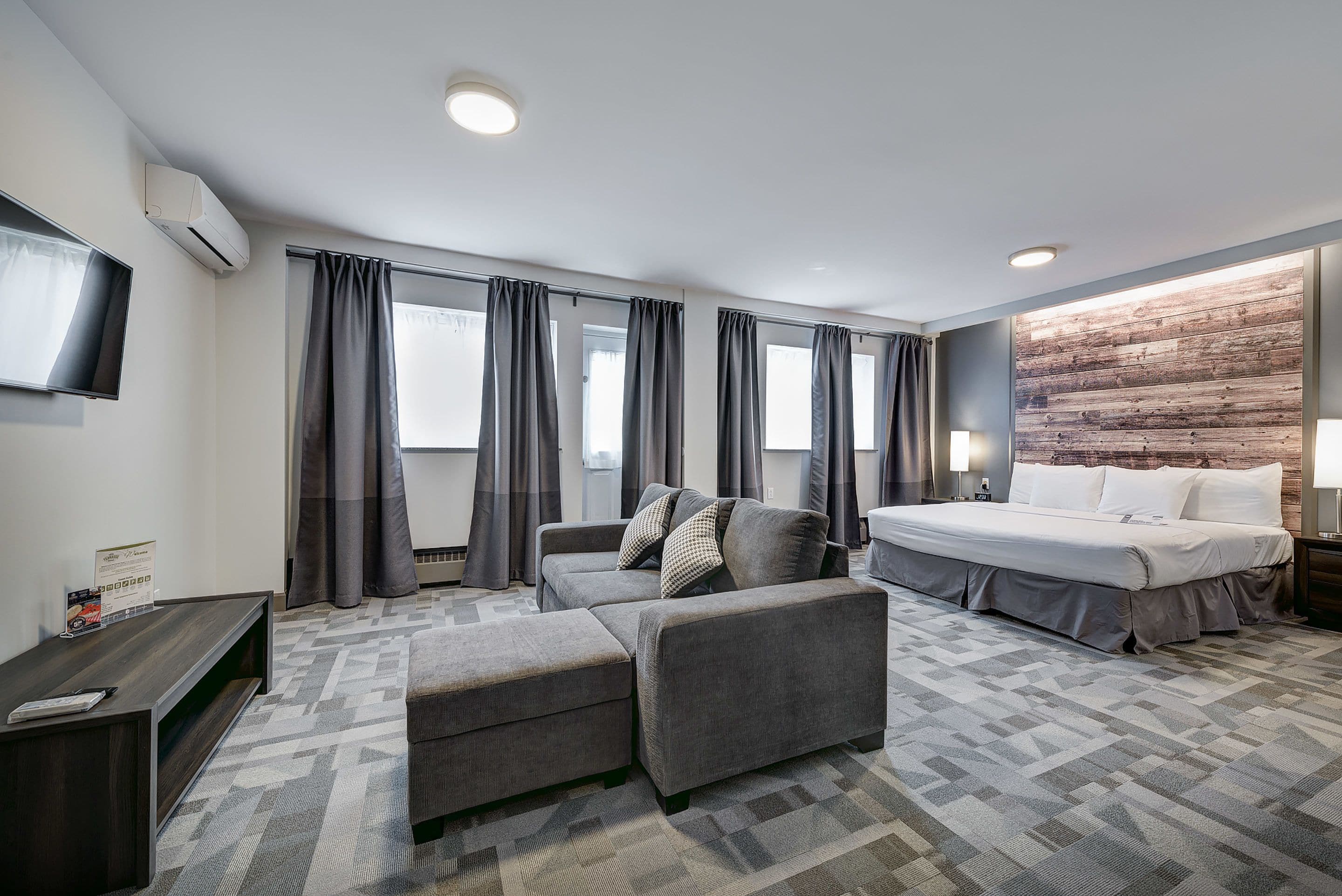 A modern hotel room with a large bed, a sofa, a TV, and a flat-screen TV mounted on the wall.