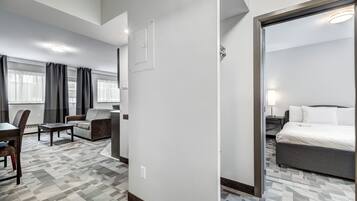 A hotel room with a bed, a desk, a chair, and a sofa. There is a window with curtains and a door.