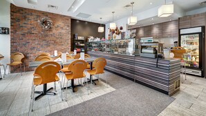 A modern restaurant with a brick wall, wooden chairs, a counter with a menu, and a refrigerator stocked with beverages. - Hotel Terrasse Royale (Montreal)