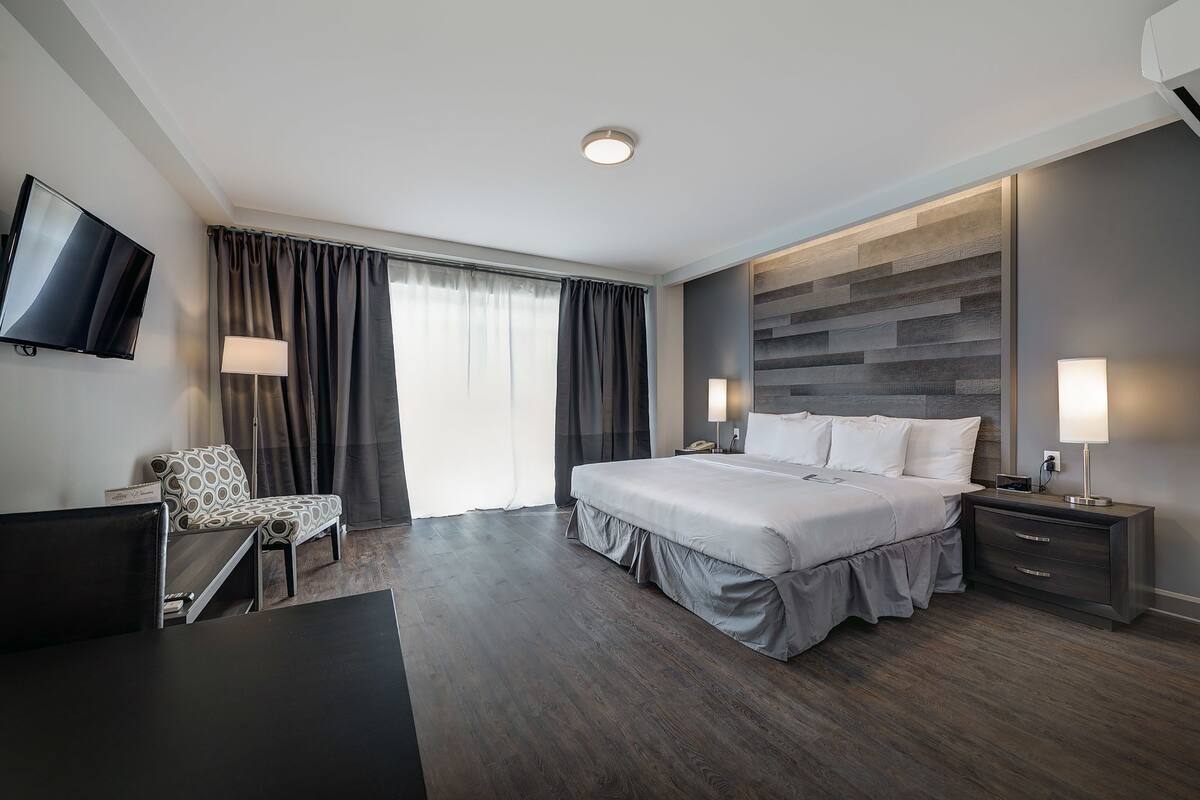 A modern hotel room with a large bed, a desk, a chair, and a TV.