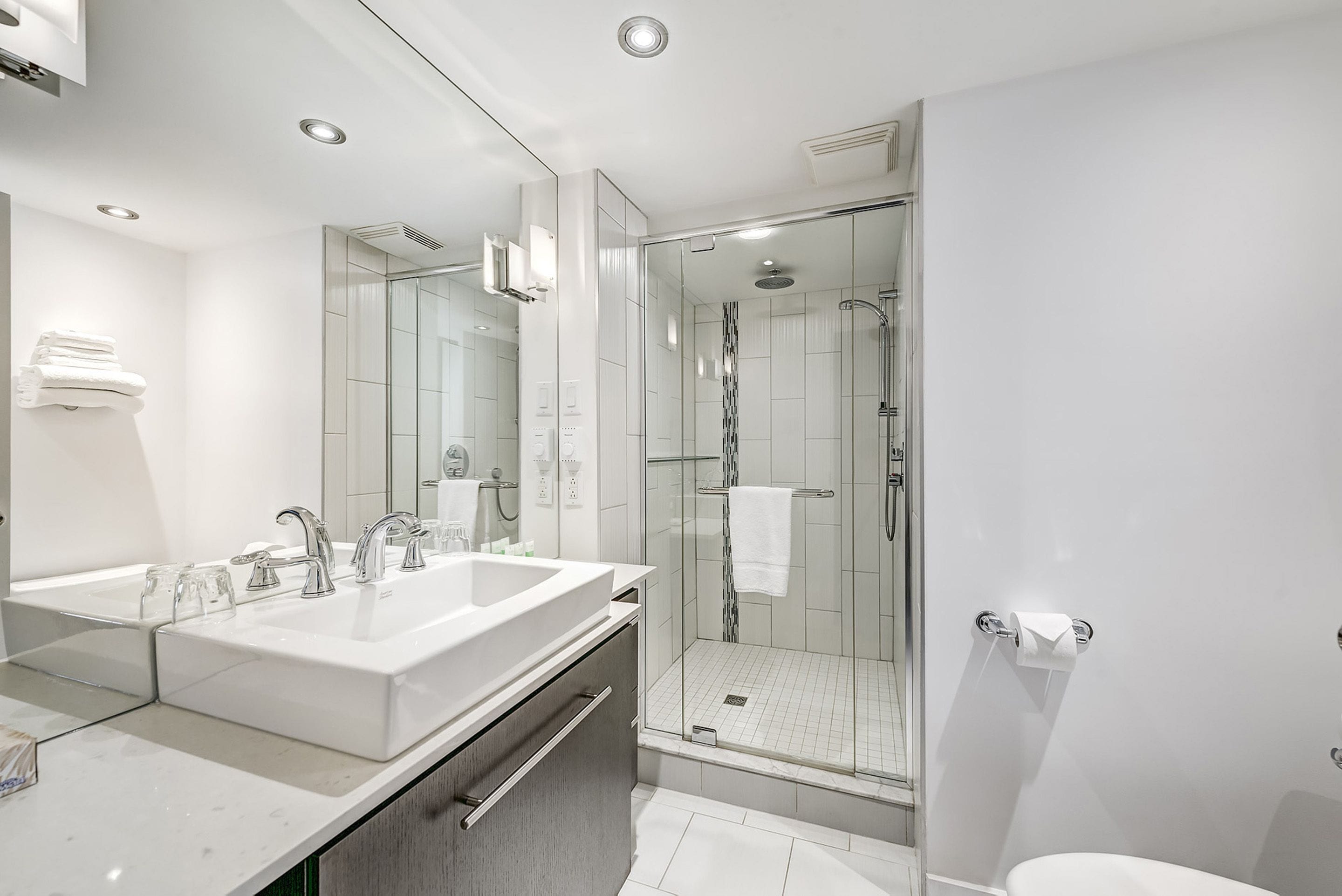 A modern bathroom with a double sink, a glass shower enclosure, and a toilet.