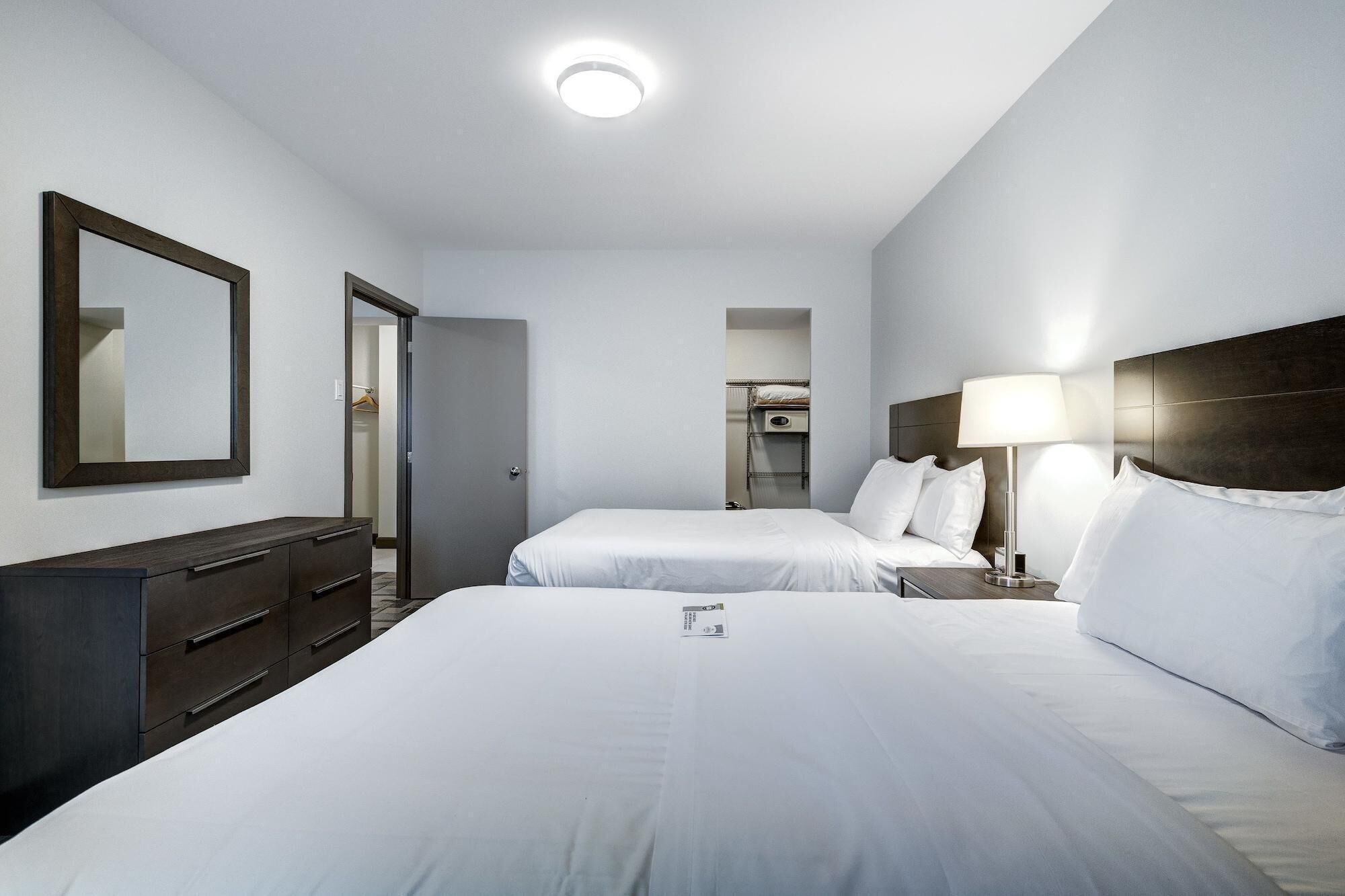 A hotel room with two beds, a dresser, a mirror, a lamp, and a ceiling light.