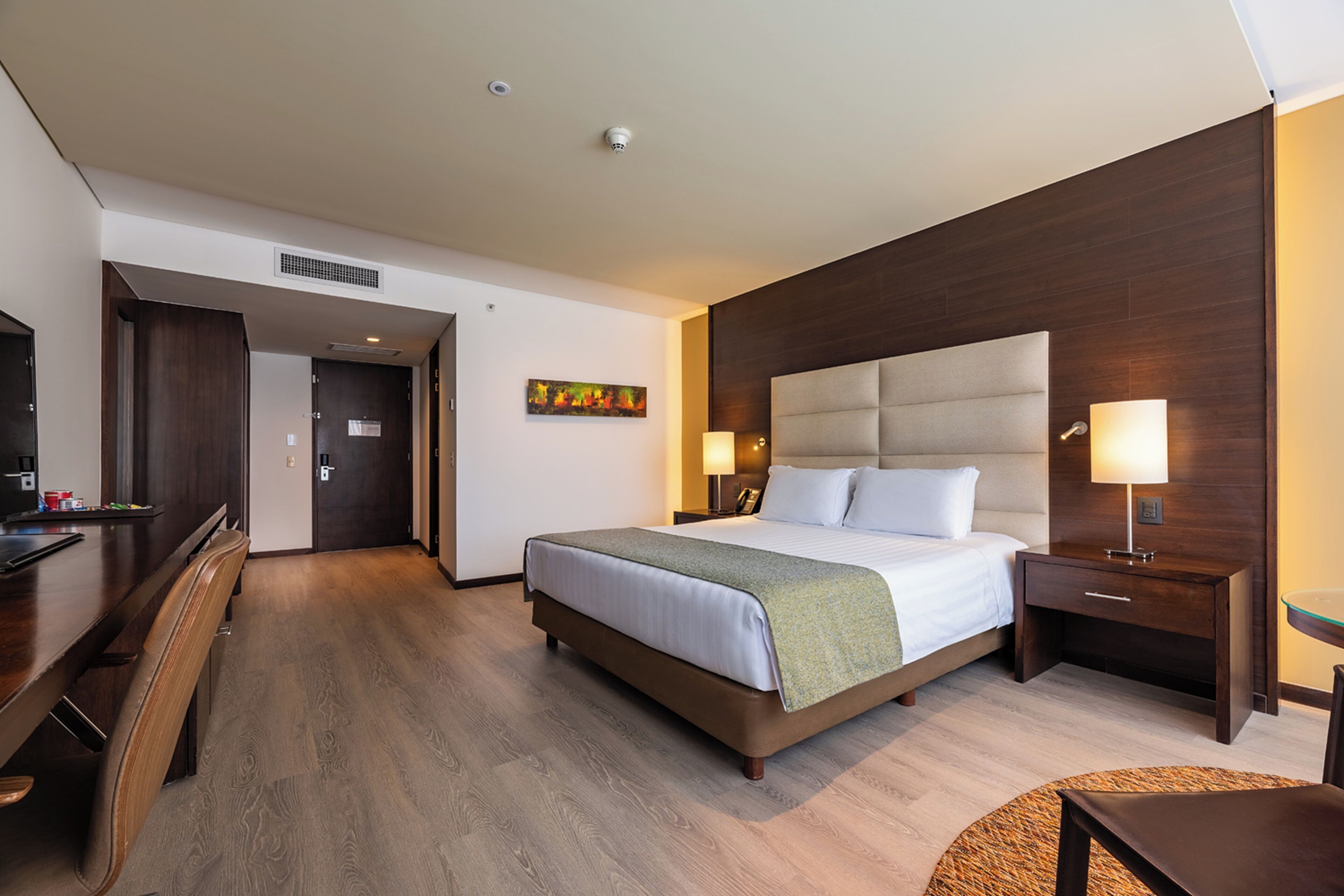 A hotel room with a bed, bedside tables, a desk, and a chair.