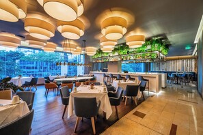 Un restaurante con varias mesas, lámparas colgantes, una zona de bar y vistas al exterior.