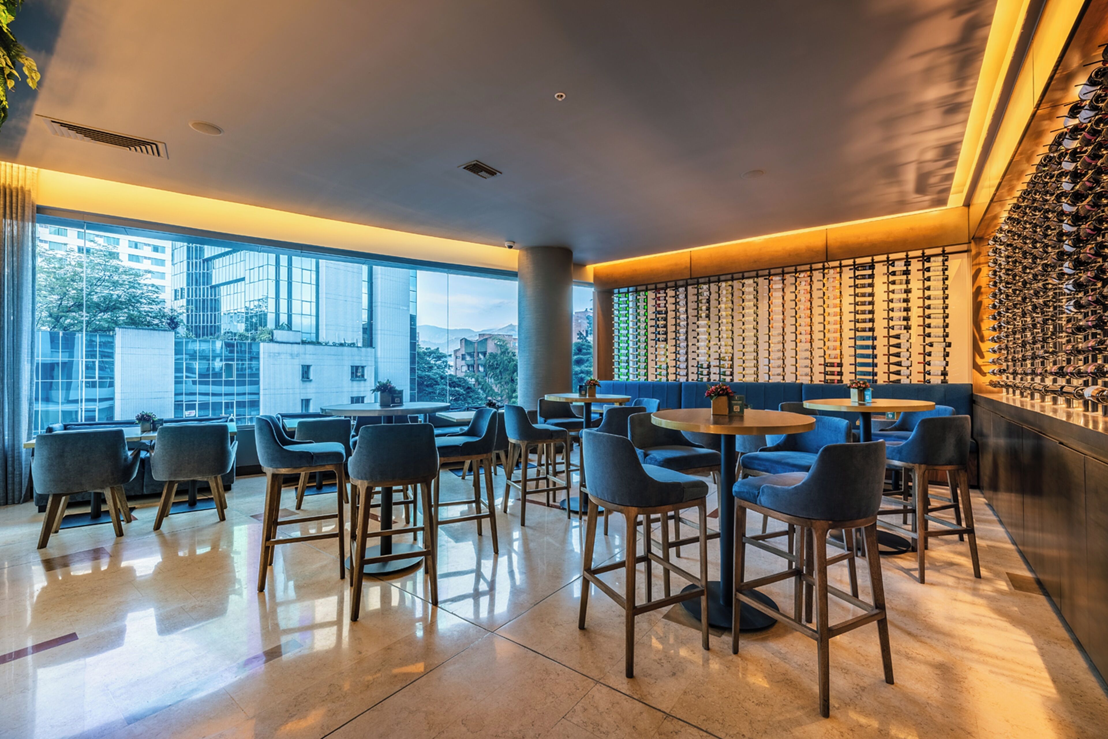 A modern interior with a bar area, seating, and a view of the cityscape.
